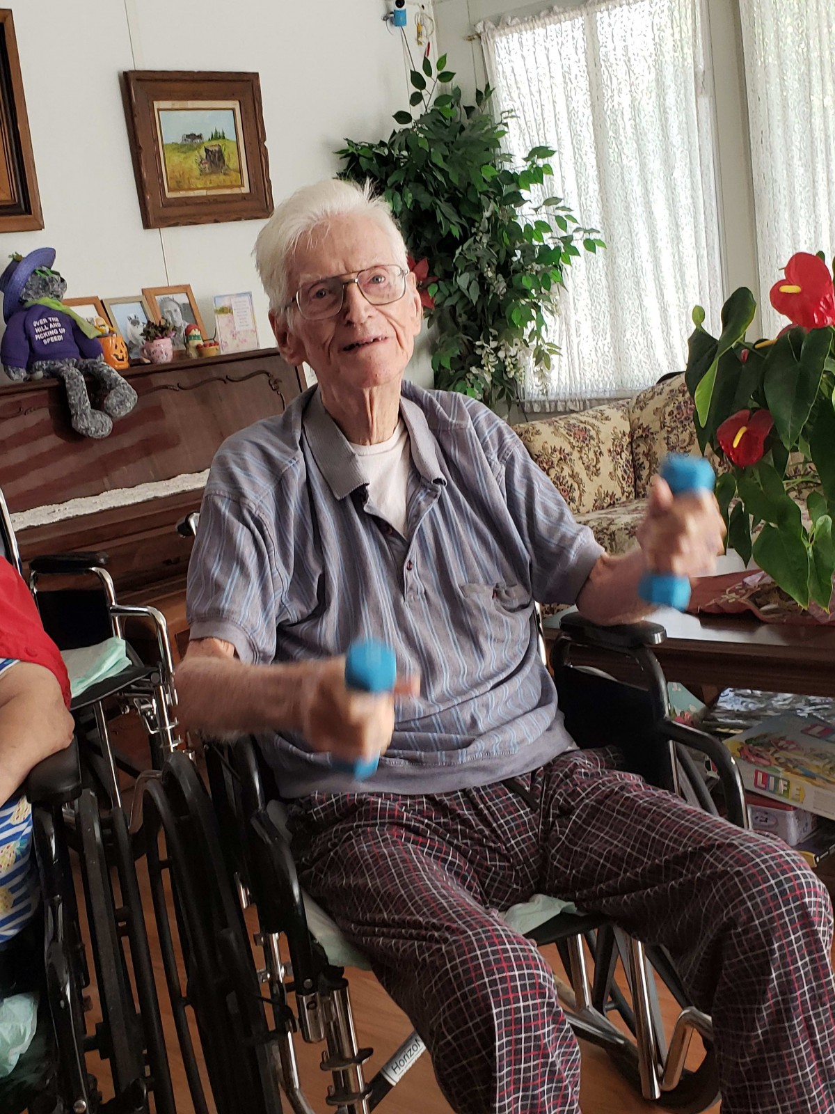 An elderly person exercising with dumbbells indoors while seated in a wheelchair.