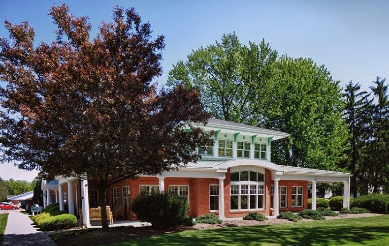 A two-story brick house with large windows surrounded by trees and a well-maintained lawn.