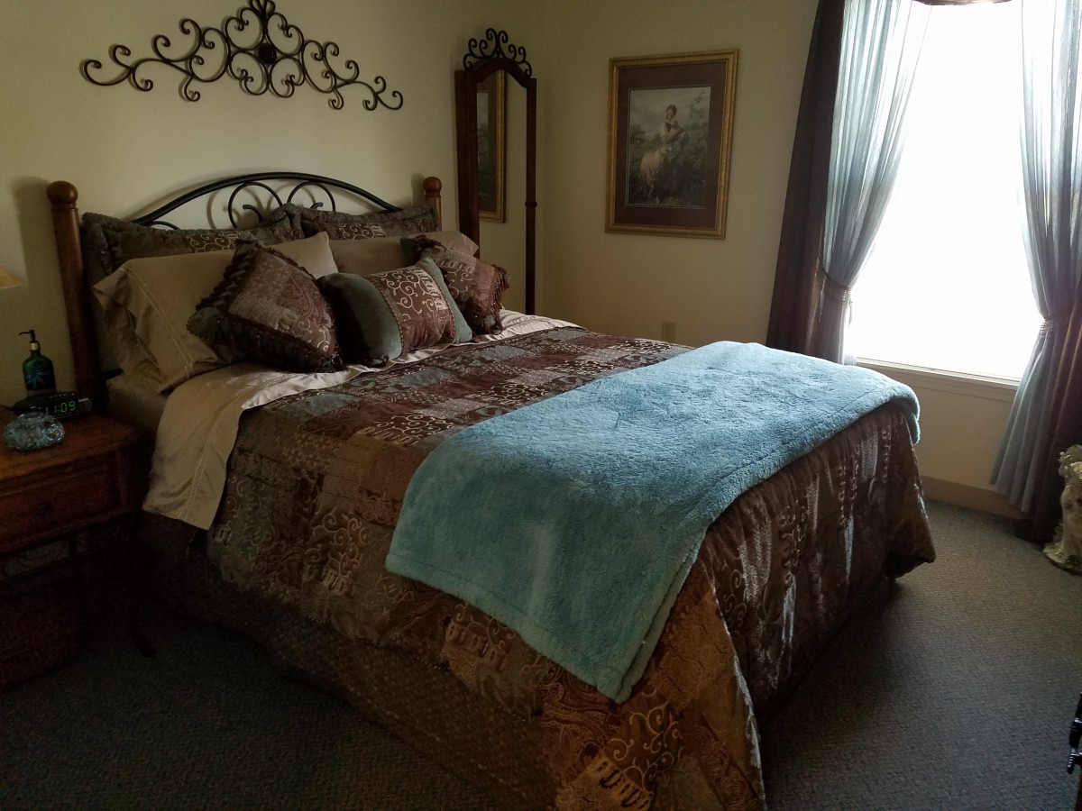A cozy and well-decorated bedroom featuring a large bed with layered bedding and pillows, complemented by a decorative mirror and artwork on the walls.