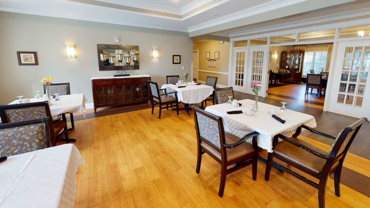 A spacious dining room with neatly arranged tables and chairs, featuring a wooden floor and warm decor.
