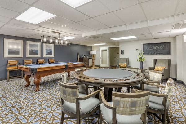 A spacious game room featuring a poker table and a pool table, with stylish chairs and decorative lighting.