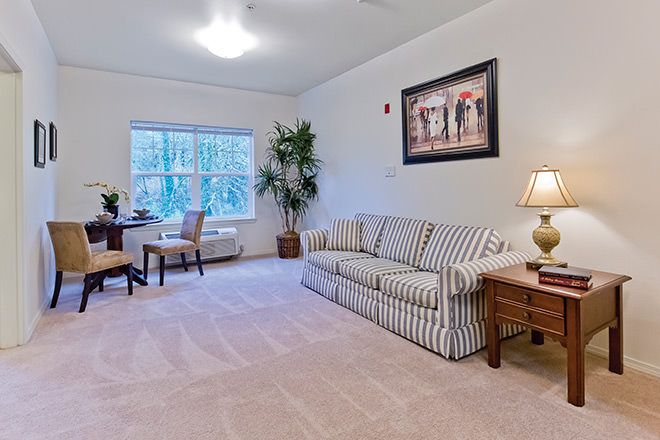 A cozy living room with a striped sofa, desk area, and large window providing natural light.