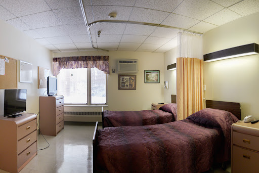 A well-furnished hospital room featuring two beds and a window with natural light.