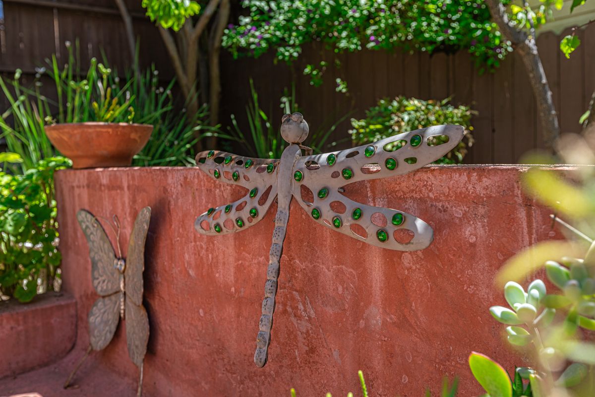 A metal dragonfly sculpture adorns a garden wall, surrounded by greenery.
