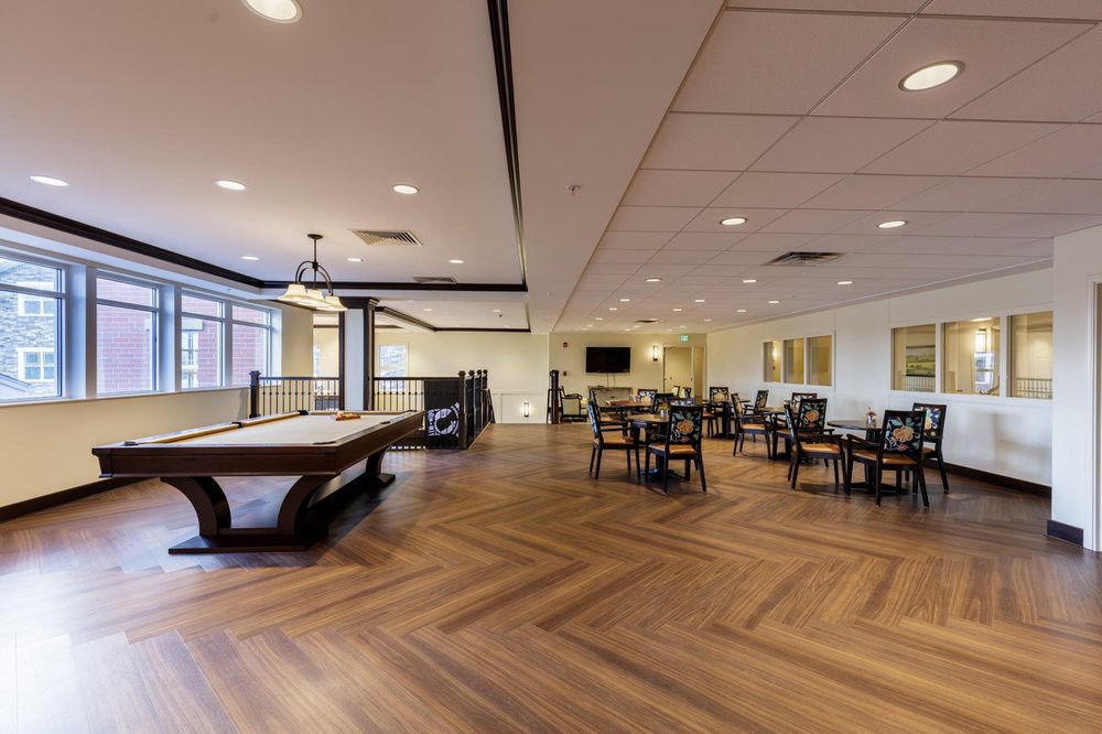 A spacious recreation area with a billiards table and seating, featuring hardwood flooring and ceiling lights.