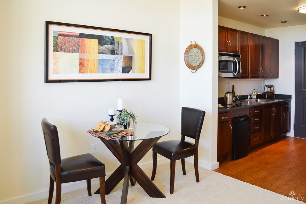 A cozy dining area with a small round table and two chairs, adjacent to a modern kitchen.