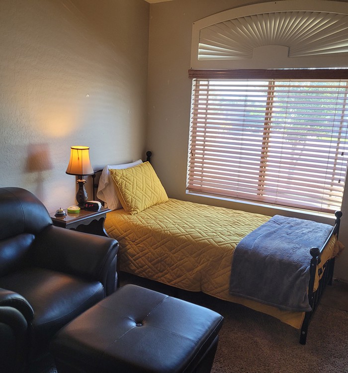 A cozy bedroom with a single bed, armchair, and window with blinds.