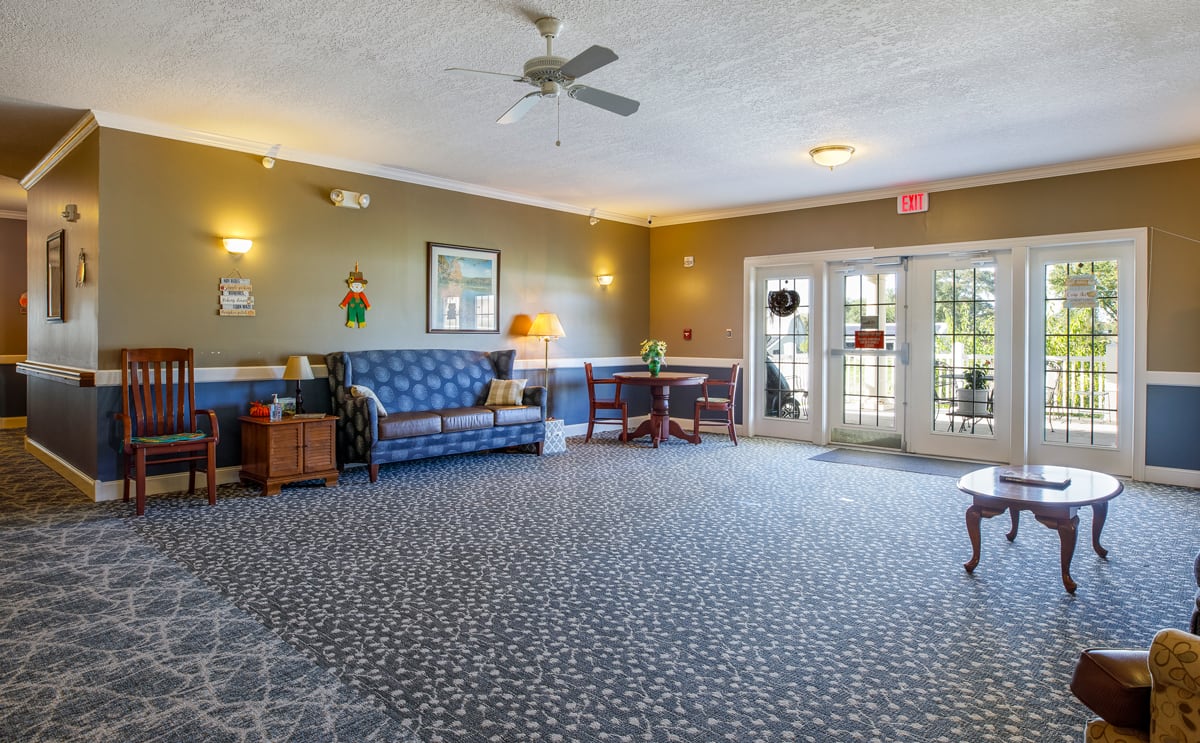 A cozy lobby area featuring a sofa and tables, with a carpeted floor and ceiling fan.