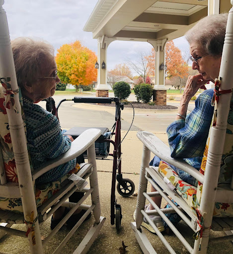 Two elderly women enjoying a peaceful moment together on a porch during autumn.