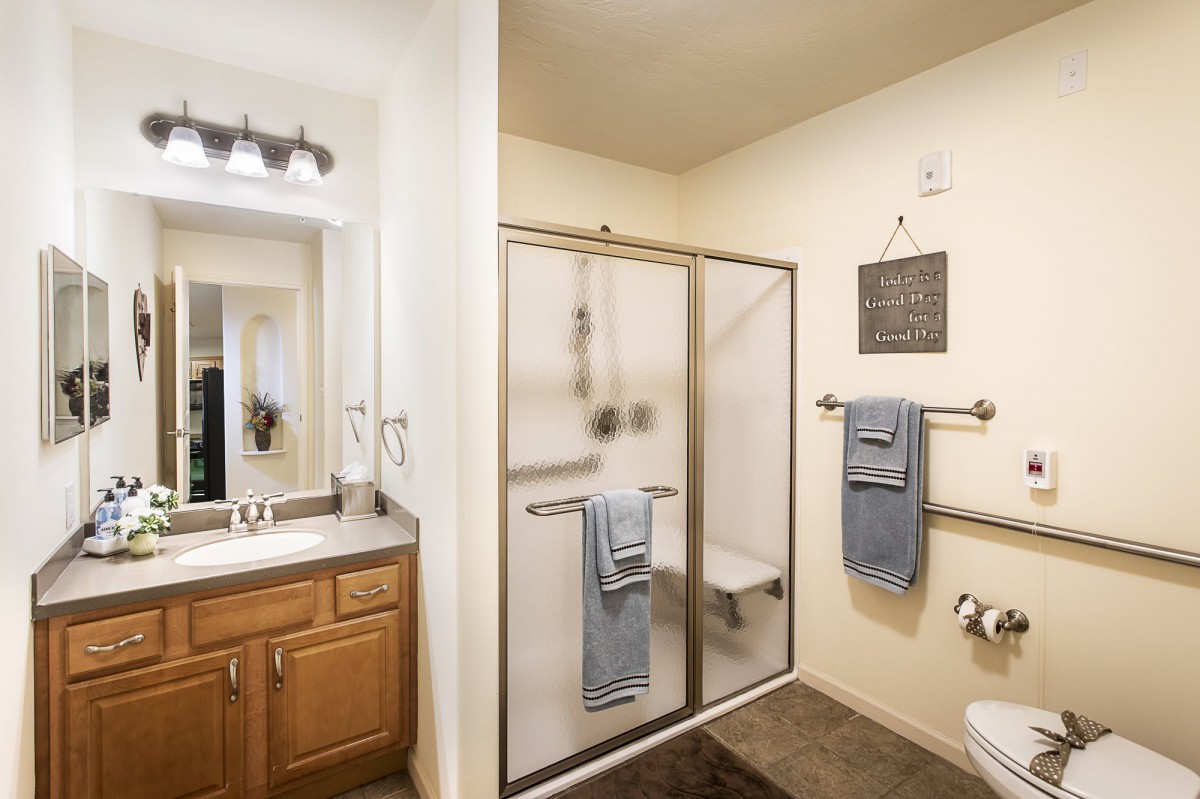 A modern bathroom with a glass shower enclosure, wooden cabinets, and neatly hung towels.
