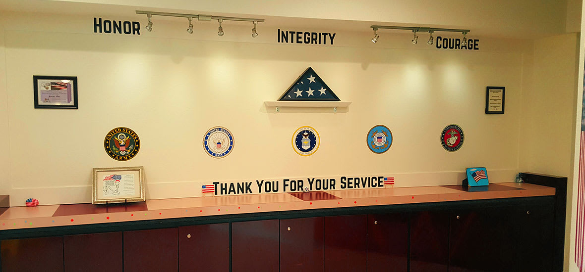 A tribute wall displaying a folded American flag and military emblems with the words 'Thank You For Your Service' and 'Integrity'.