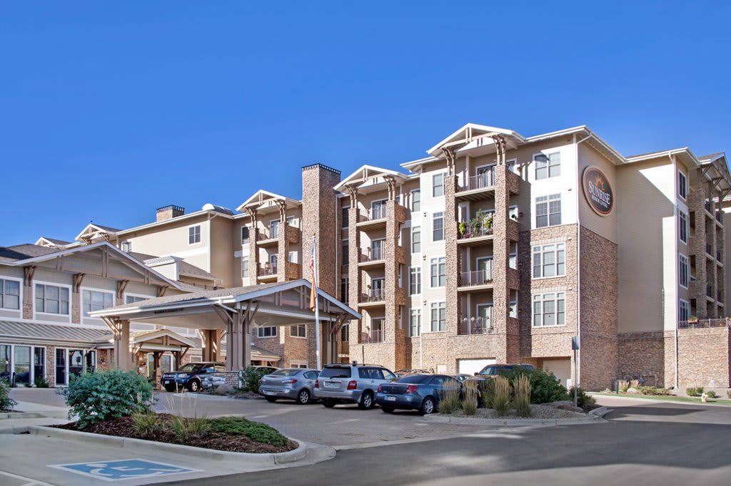 A modern apartment complex with a parking area under a clear blue sky.