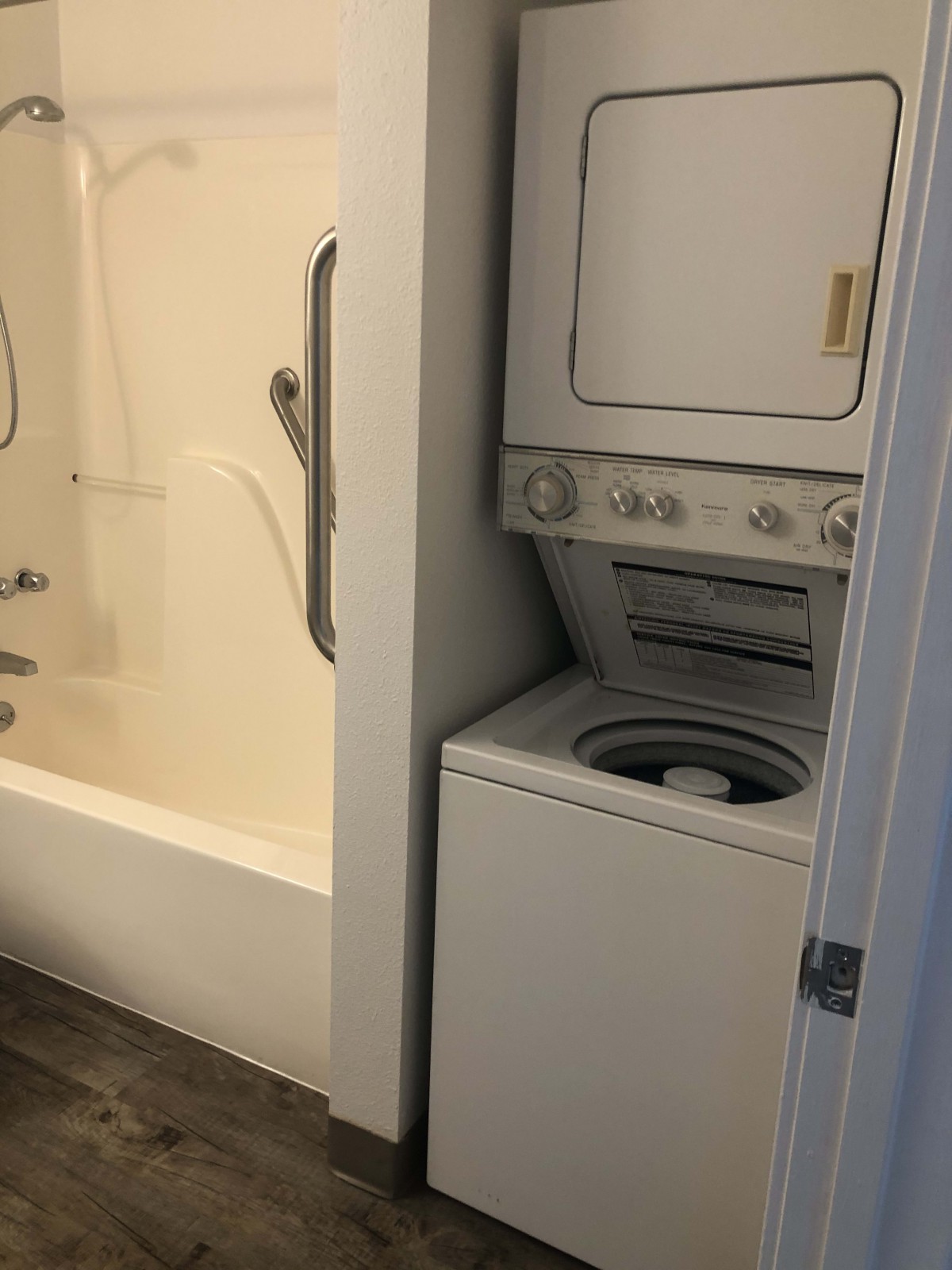 A compact bathroom space featuring a stacked washer and dryer next to a bathtub.