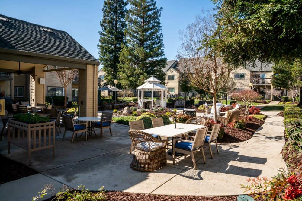 A sunny outdoor patio area with tables, chairs, and a gazebo surrounded by landscaped greenery.
