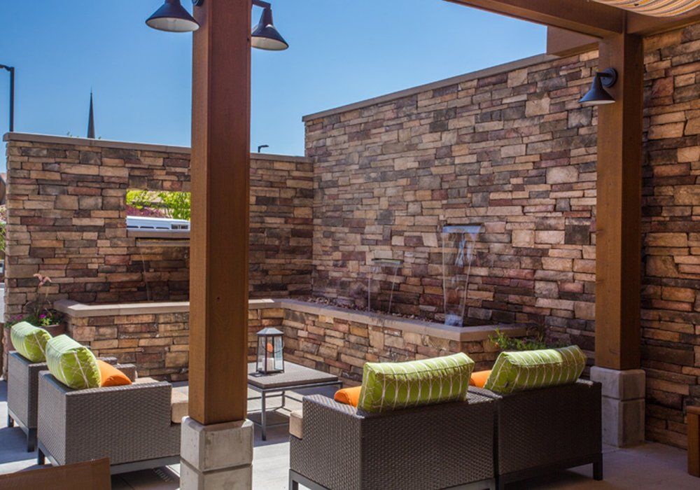 A cozy outdoor patio with cushioned seating and a stone wall under a clear blue sky.