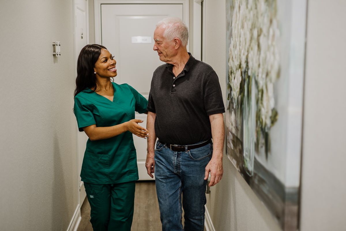 A nurse assists an elderly patient in a hallway, providing supportive care.