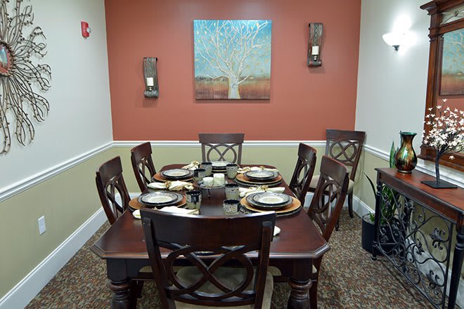 A neatly set dining table with six chairs in a warmly decorated room featuring wall art and candles.