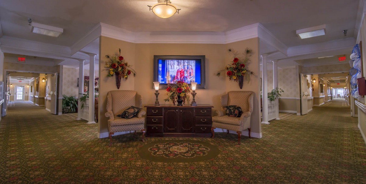 A traditional living room setup featuring a television, elegant chairs, and floral decorations.