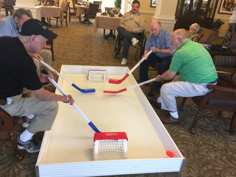 Elderly men enjoy a friendly game of table hockey indoors.