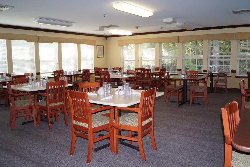 An empty dining room with neatly arranged tables and chairs, lit by natural light.