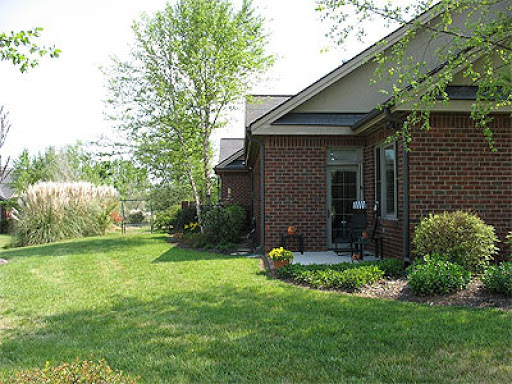 A serene view of a brick house surrounded by a lush green lawn and garden.