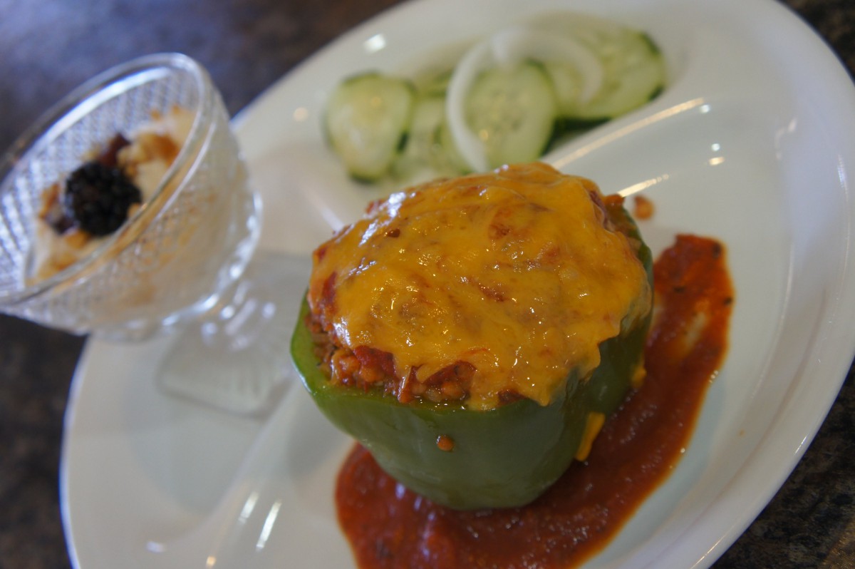A stuffed green bell pepper topped with melted cheese, served alongside cucumber slices and a creamy dessert.