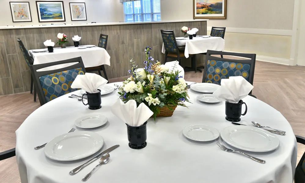 An elegantly set dining table with a floral centerpiece and neatly arranged white napkins.