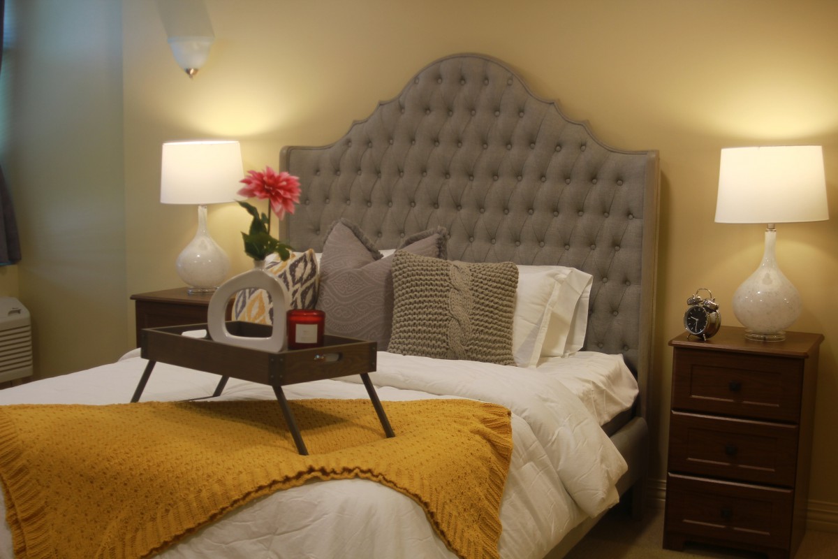 A cozy bedroom with a tufted headboard, decorative pillows, and a tray with flowers on the bed.