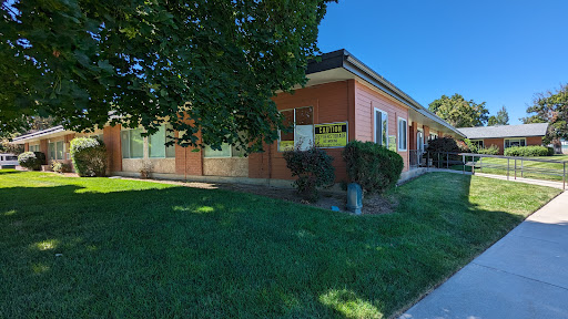 A sunny day view of a building surrounded by green grass and trees.