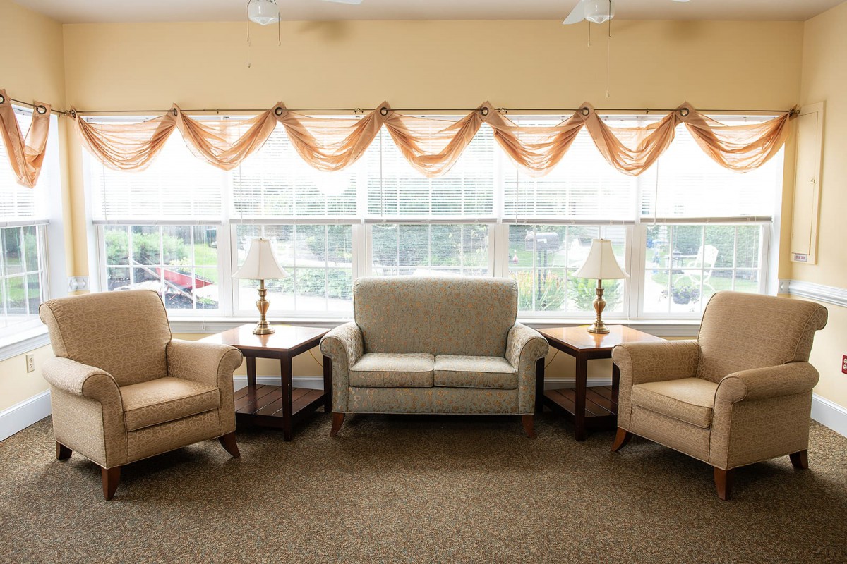 A cozy living room setup with a sofa, two armchairs, and lamps by large windows.