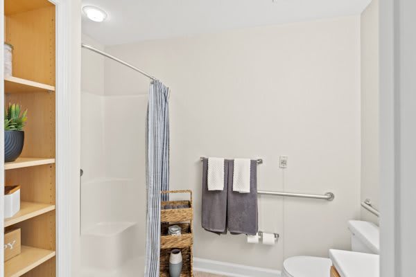 A minimalist bathroom with a shower, neatly arranged towels, and a storage shelf.
