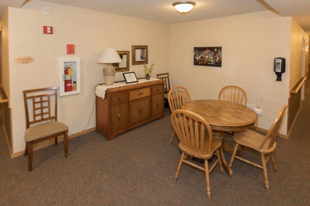 A cozy dining room with a wooden table and chairs, decorated with artwork and a sideboard with a lamp.