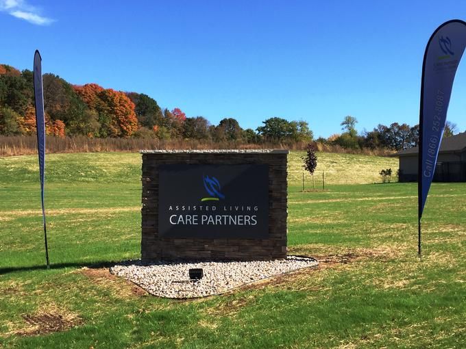 A stone sign stands in a grassy field with trees in the background under a clear blue sky.