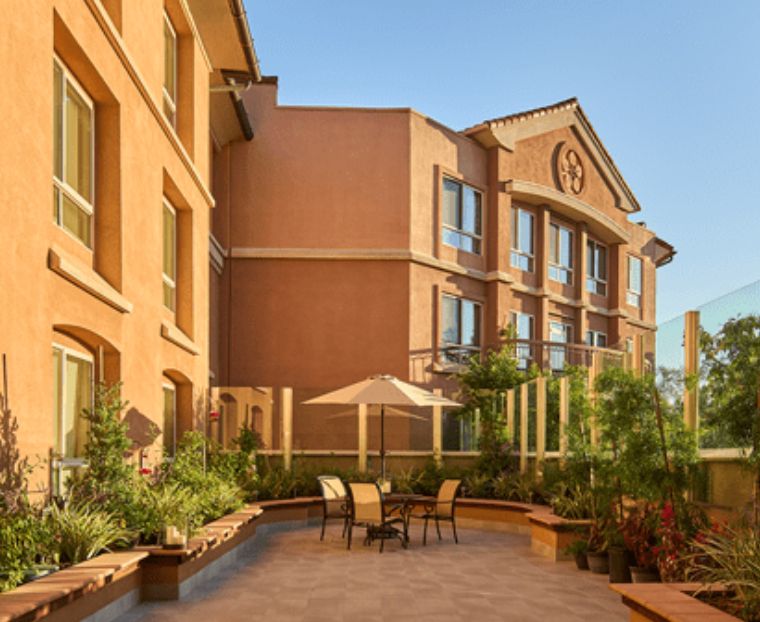 A sunny patio area outside a hotel building with outdoor seating and lush greenery.