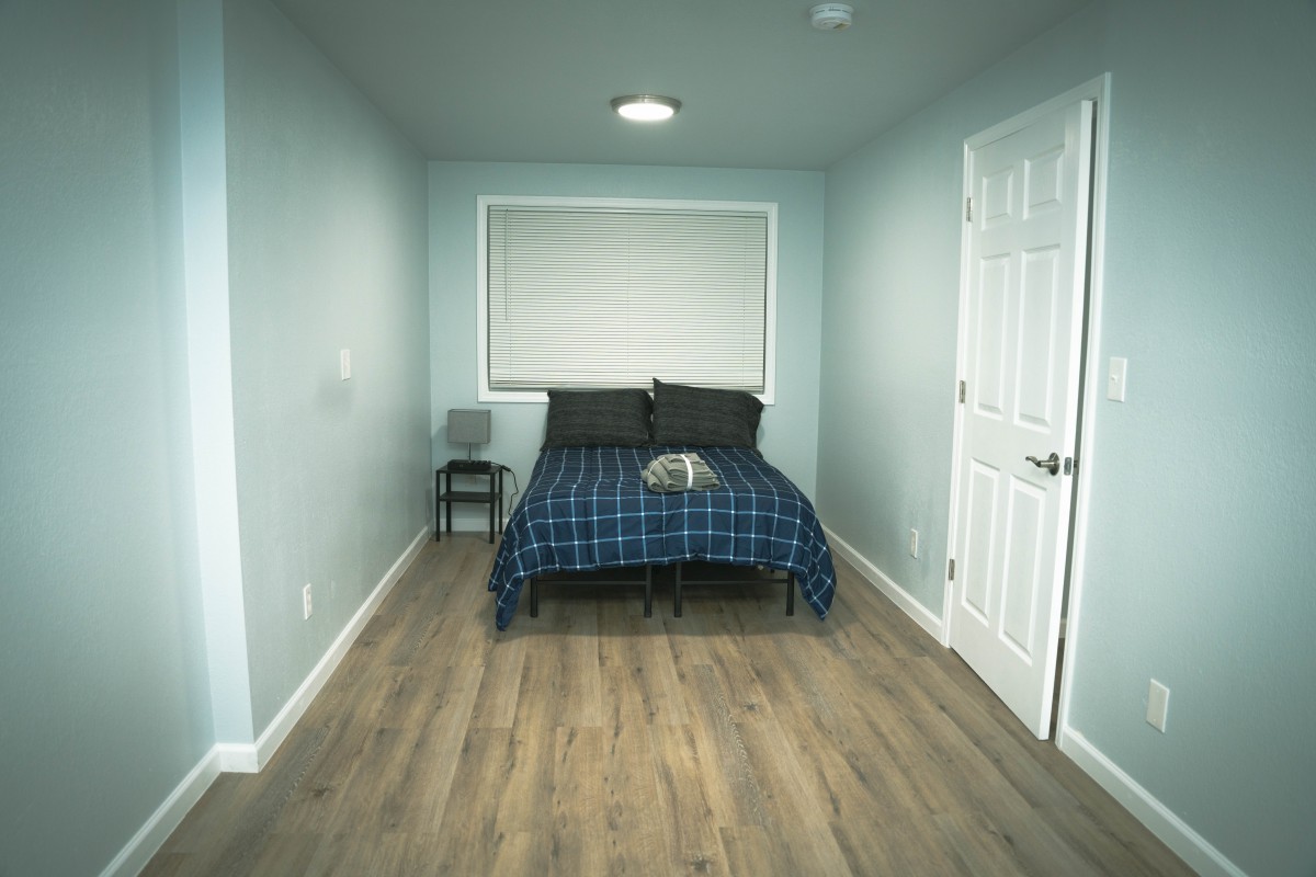 A small, minimalist bedroom with blue bedding and a wooden floor.