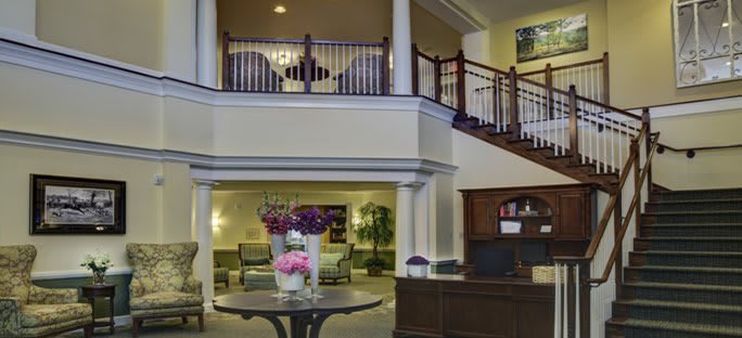 A beautifully designed hotel lobby featuring a reception desk, elegant staircase, and comfortable seating area adorned with floral arrangements.