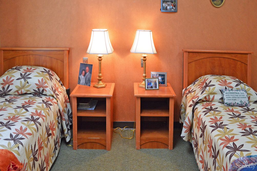 A cozy bedroom with twin beds, each flanked by nightstands topped with lamps and framed photos.