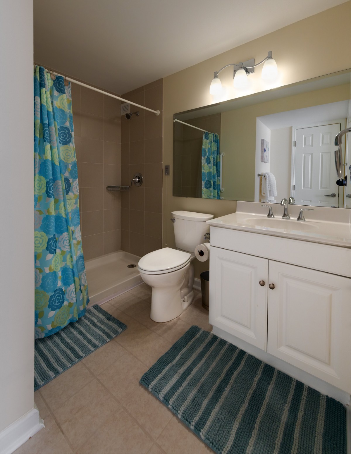 A clean and modern bathroom featuring a white vanity with a large mirror, a toilet, and a shower area with a colorful curtain.