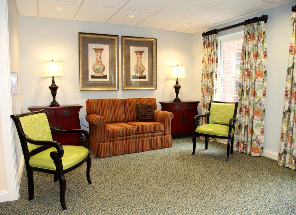 A cozy living room with a sofa, two green chairs, and decorative lamps beside framed artwork.