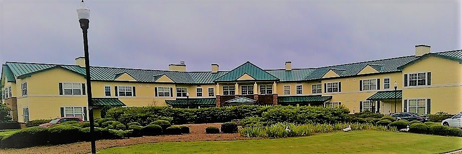 A large building with a green roof surrounded by well-maintained shrubs under a cloudy sky.