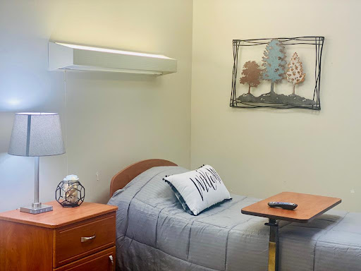 A cozy hospital room featuring a neatly made bed, bedside lamp, and decorative wall art.