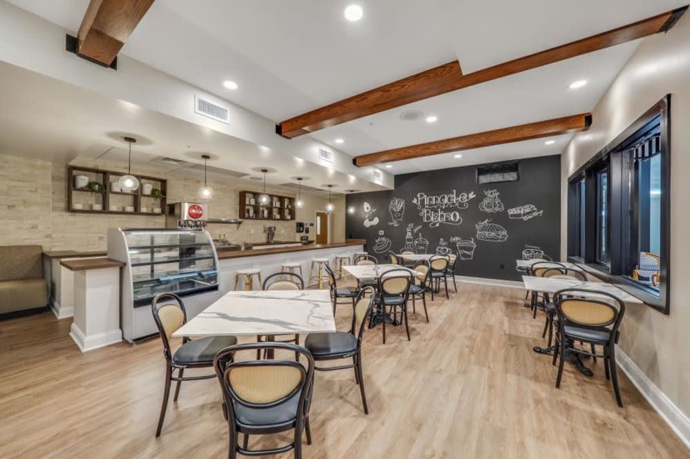 A modern cafe interior featuring wooden floors, various seating arrangements, and a decorative chalkboard wall.