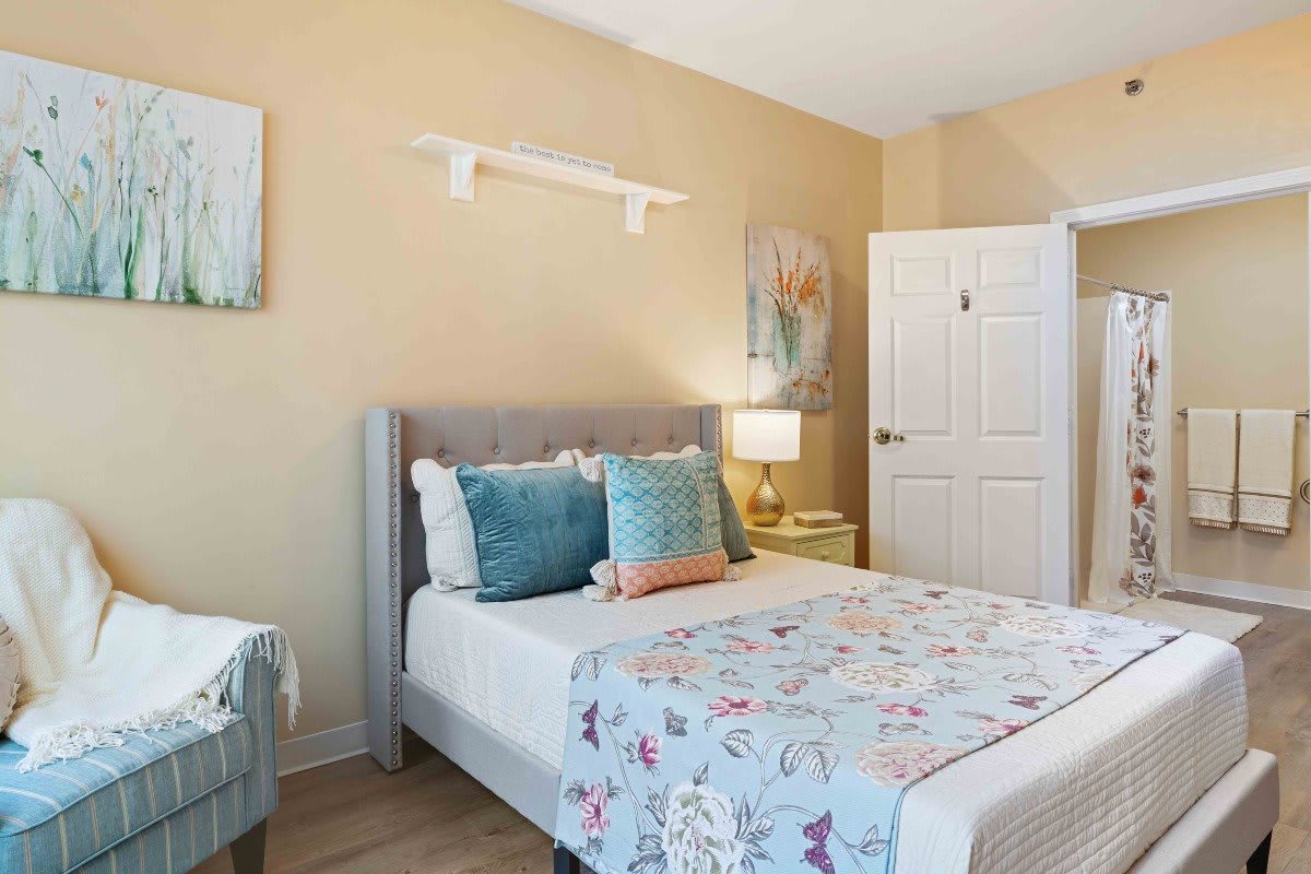 A cozy bedroom with a stylish decor featuring a bed adorned with a floral bedspread and decorative pillows, complemented by a bedside lamp.