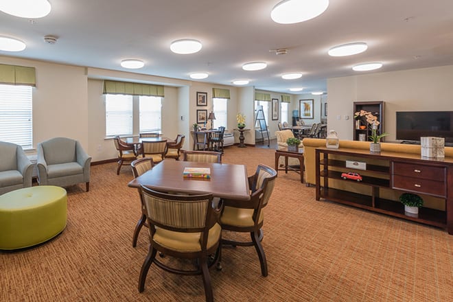 A spacious, well-lit room with multiple tables and chairs arranged for communal activities.