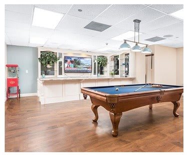 A spacious game room featuring a pool table with a wooden floor and modern lighting.