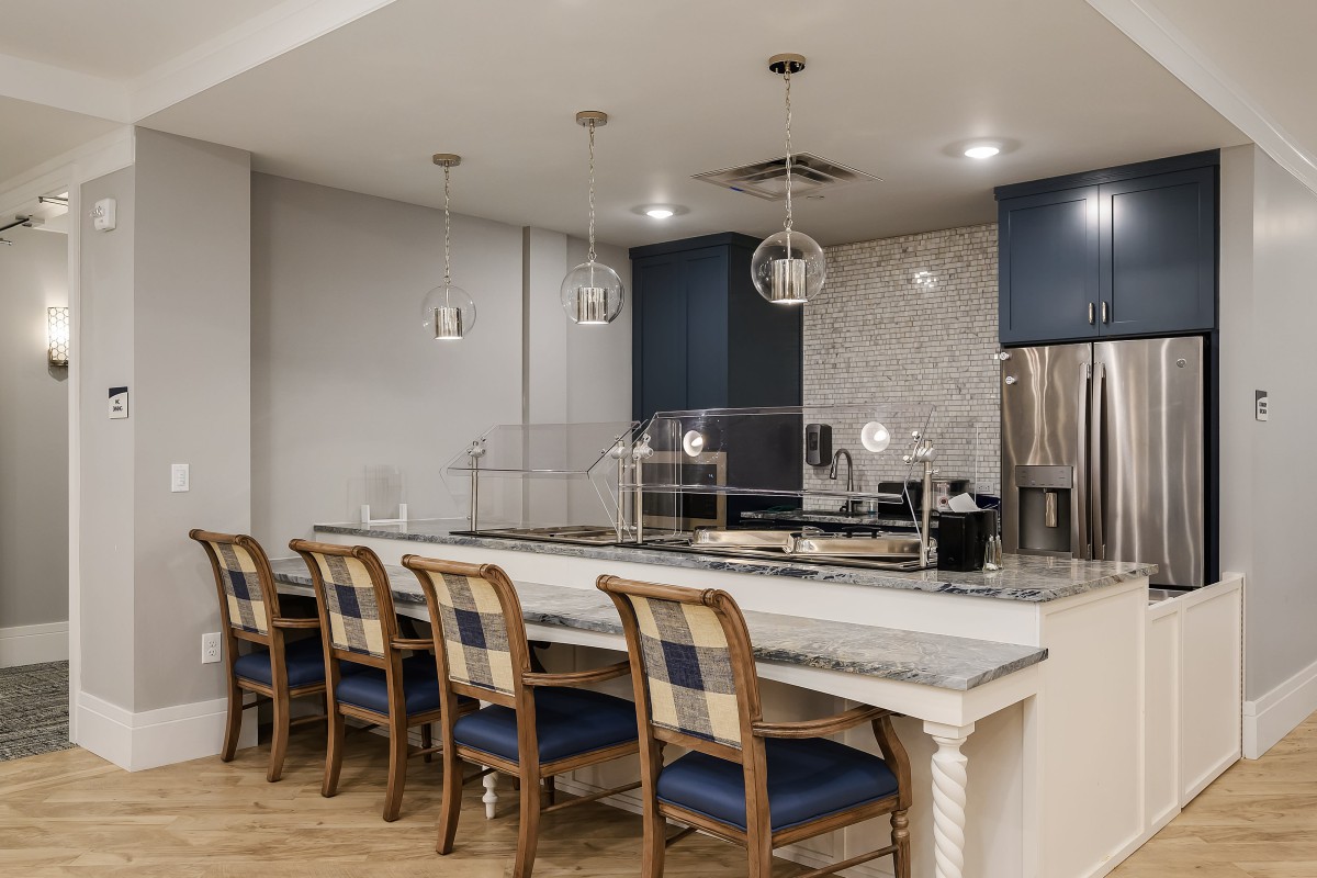 A modern kitchen interior featuring a long countertop with wooden bar stools and pendant lighting.