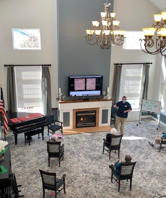A spacious room with a television, fireplace, and piano, where several people are seated for an event.