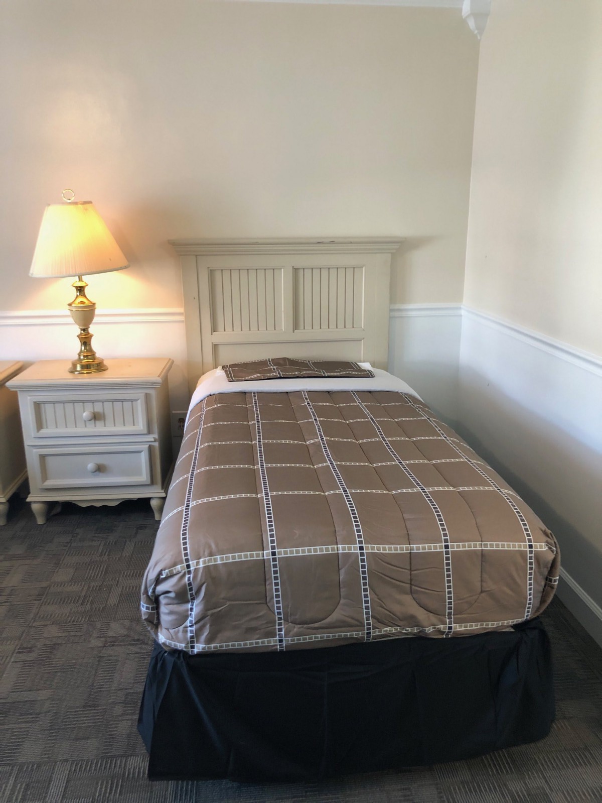 A cozy bedroom with a single bed, nightstand, and lamp.