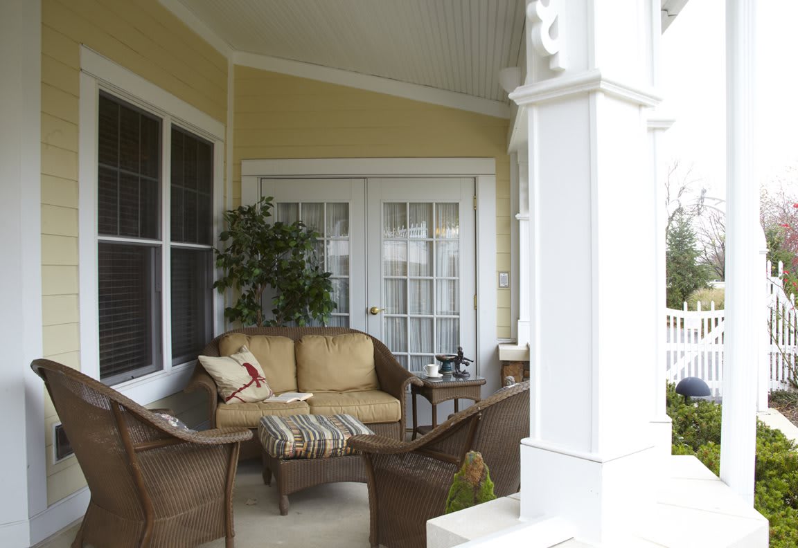 A cozy porch with wicker chairs, a couch, and potted plants creates an inviting outdoor seating area.