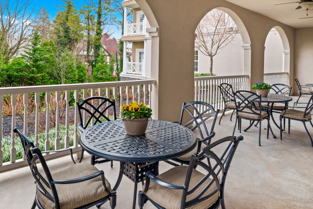 A cozy balcony with outdoor furniture and a potted plant, overlooking lush greenery and nearby buildings.